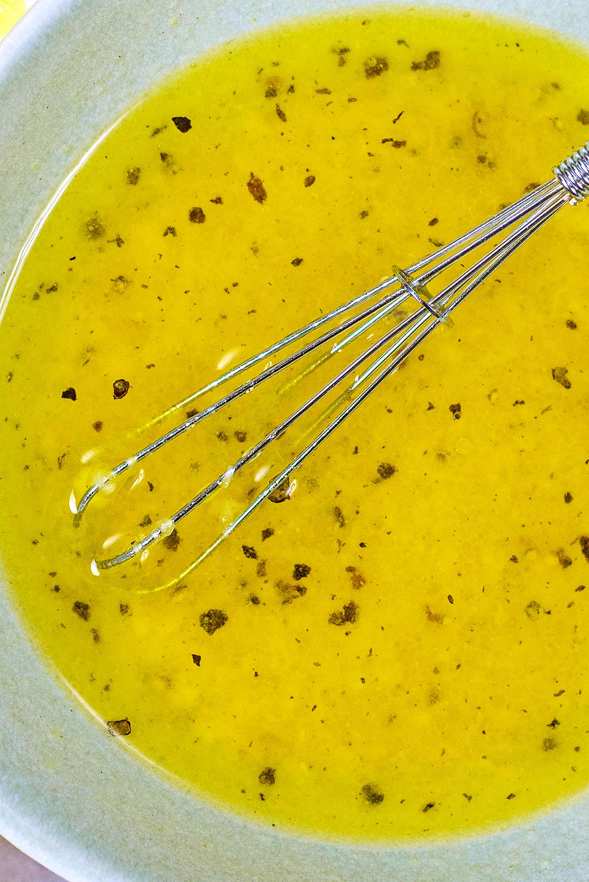 A small whisk in a bowl of salad dressing.