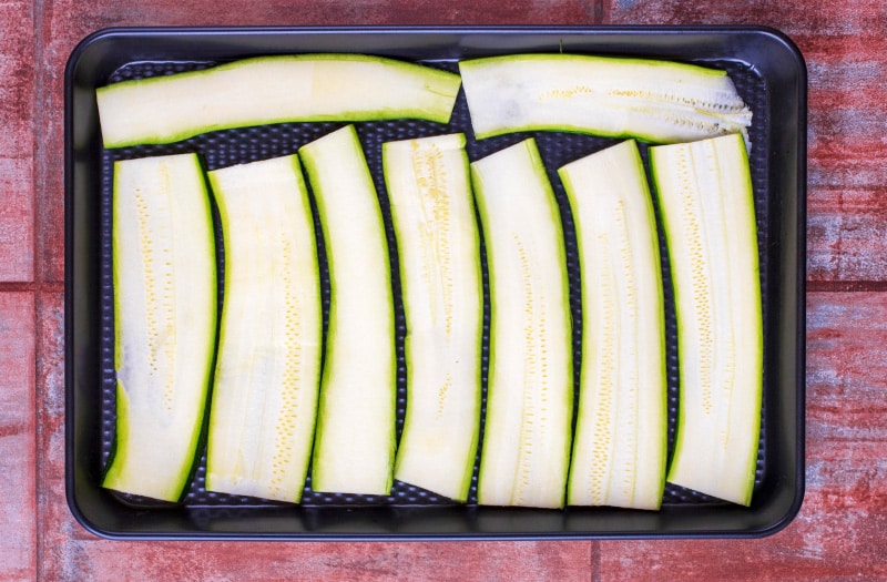 Strips of zucchini laid out on a black baking tray.
