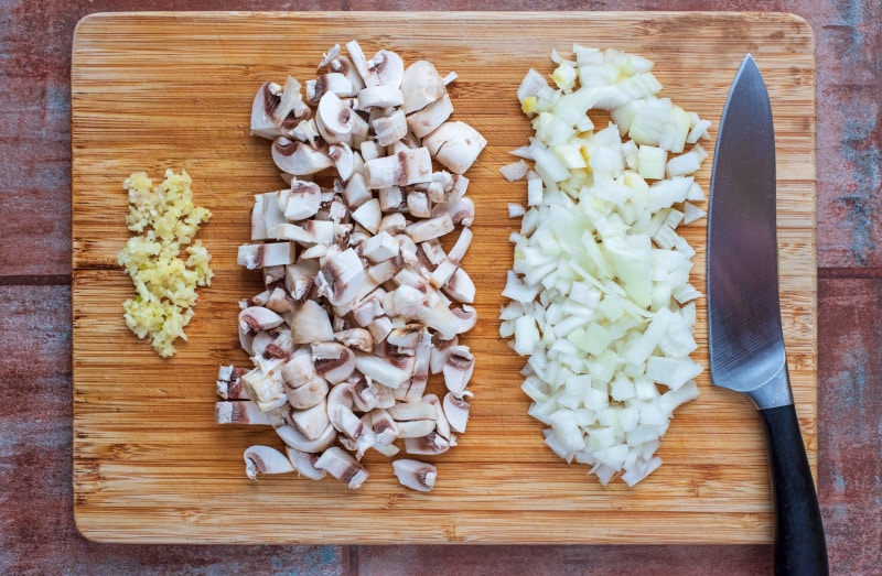 Chopped onion, mushrooms and garlic on a wooden chopping board.