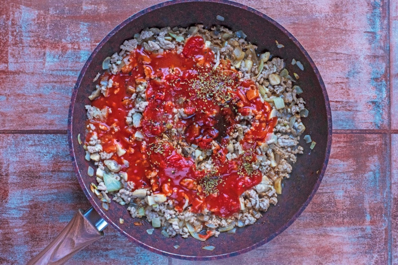 Chopped onion, mushrooms, ground turkey, garlic and pasta sauce in a frying pan.