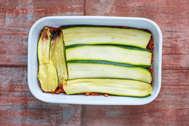 A baking dish containing a tomato meat sauce and strips of cooked zucchini.
