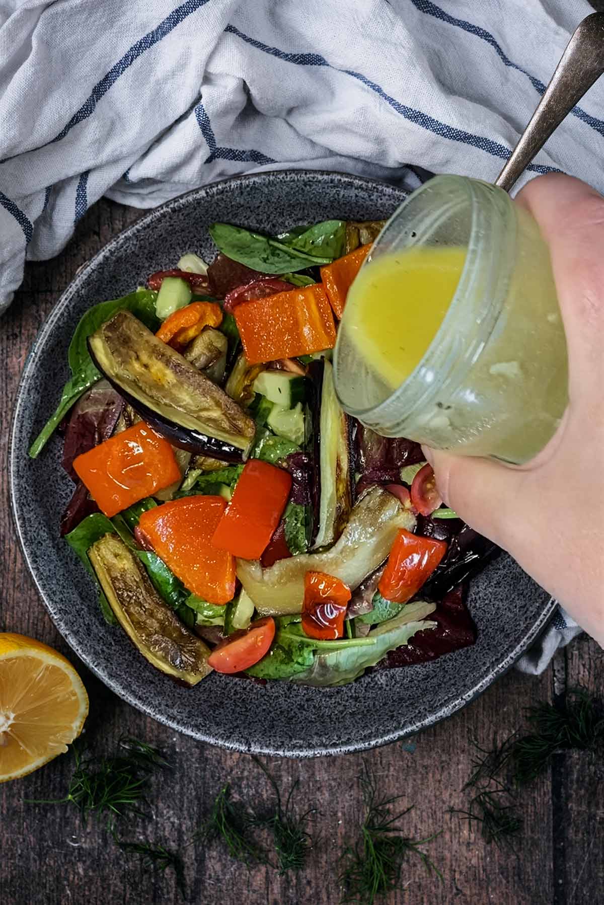 A jar of lemon vinaigrette being poured over a bowl of salad.
