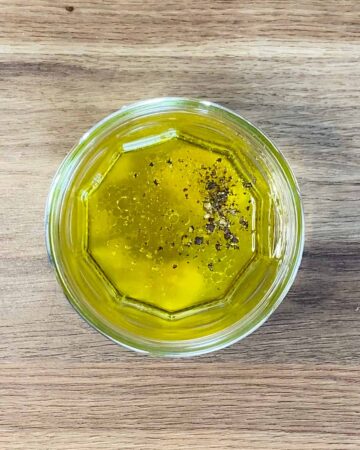 A glass jar containing oil, lemon juice, mustard and seasoning.