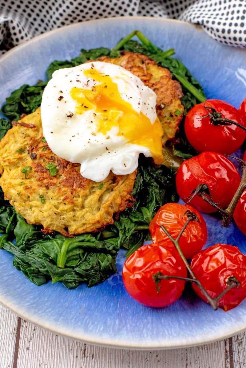 Oven Baked Hash Browns with a poached egg, spinach and cherry tomatoes, all on a blue plate.
