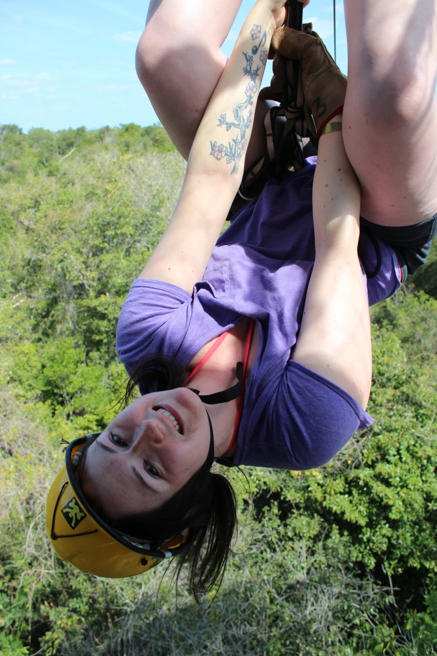 A woman zip lining upside down over trees.