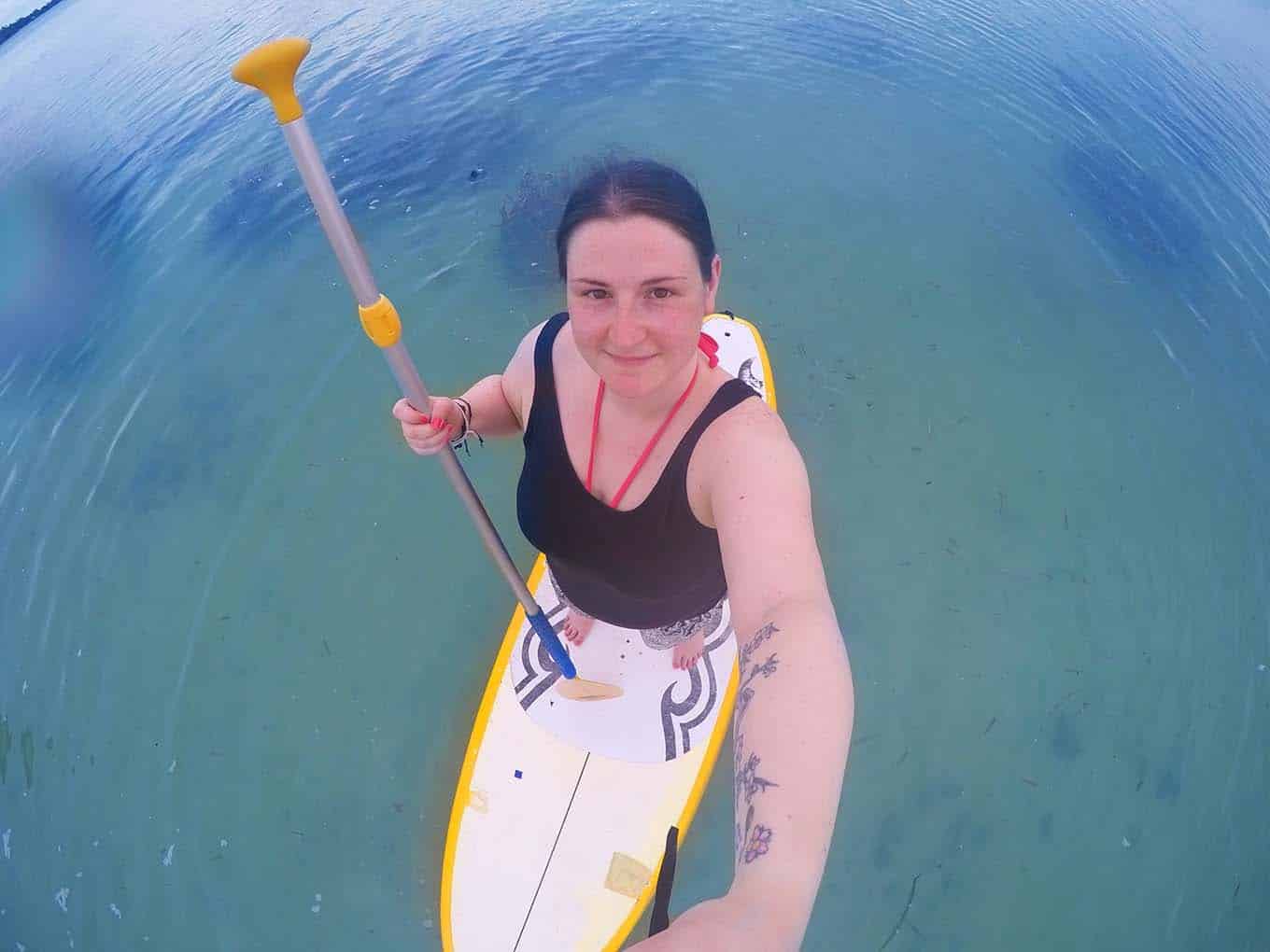 A woman taking a selfie while stood on a Paddle Board.