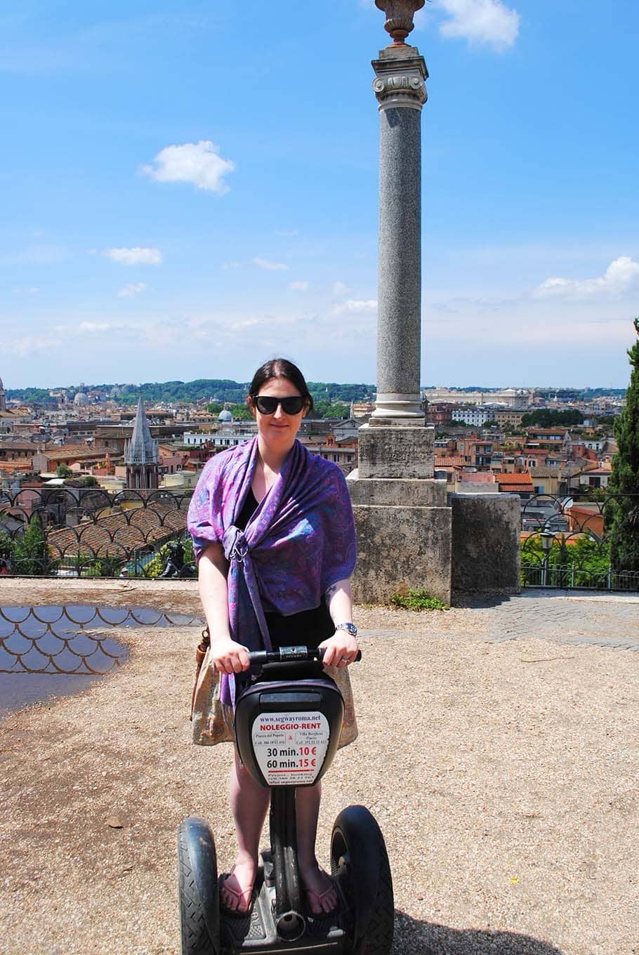 A woman riding a Segway with a city skyline in the background.
