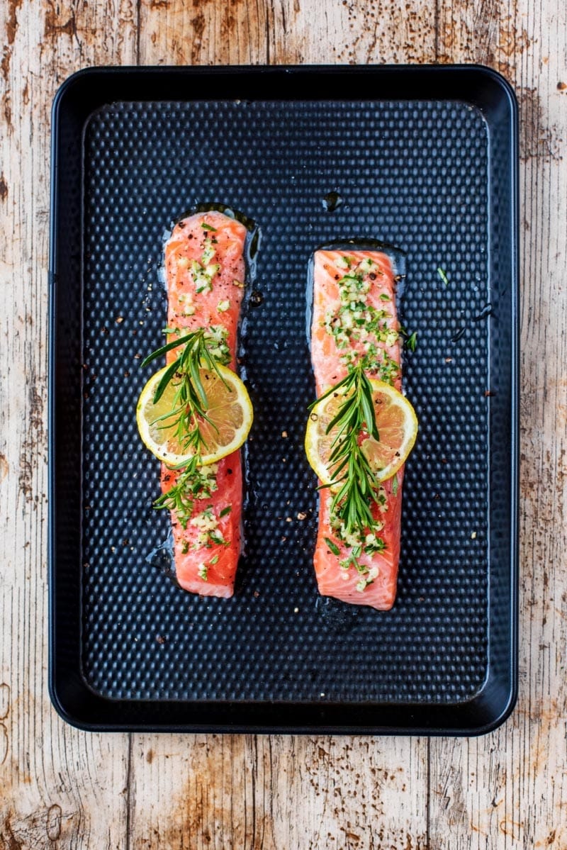 Two salmon fillets on a baking tray with lemon and rosemary