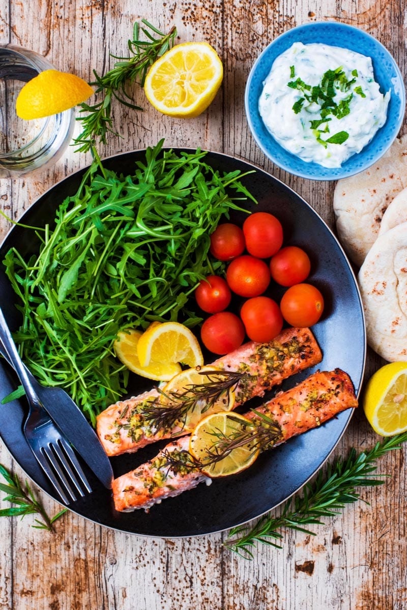 Lemon and Rosemary Salmon on a black plate with tomatoes and salad