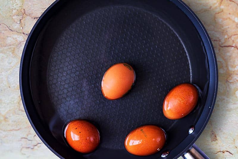 A frying pan full of water with four whole eggs in it.