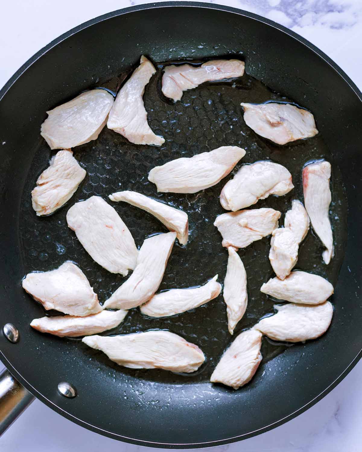 A frying pan with chunks of chicken breast cooking in it.