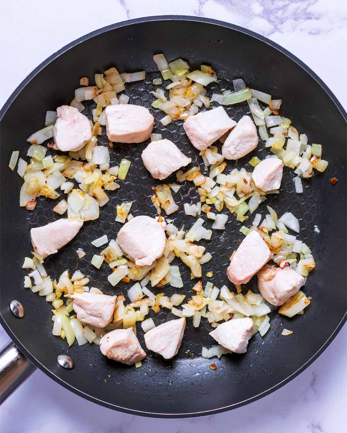 Chunks of chicken and chopped onion cooking in a frying pan.