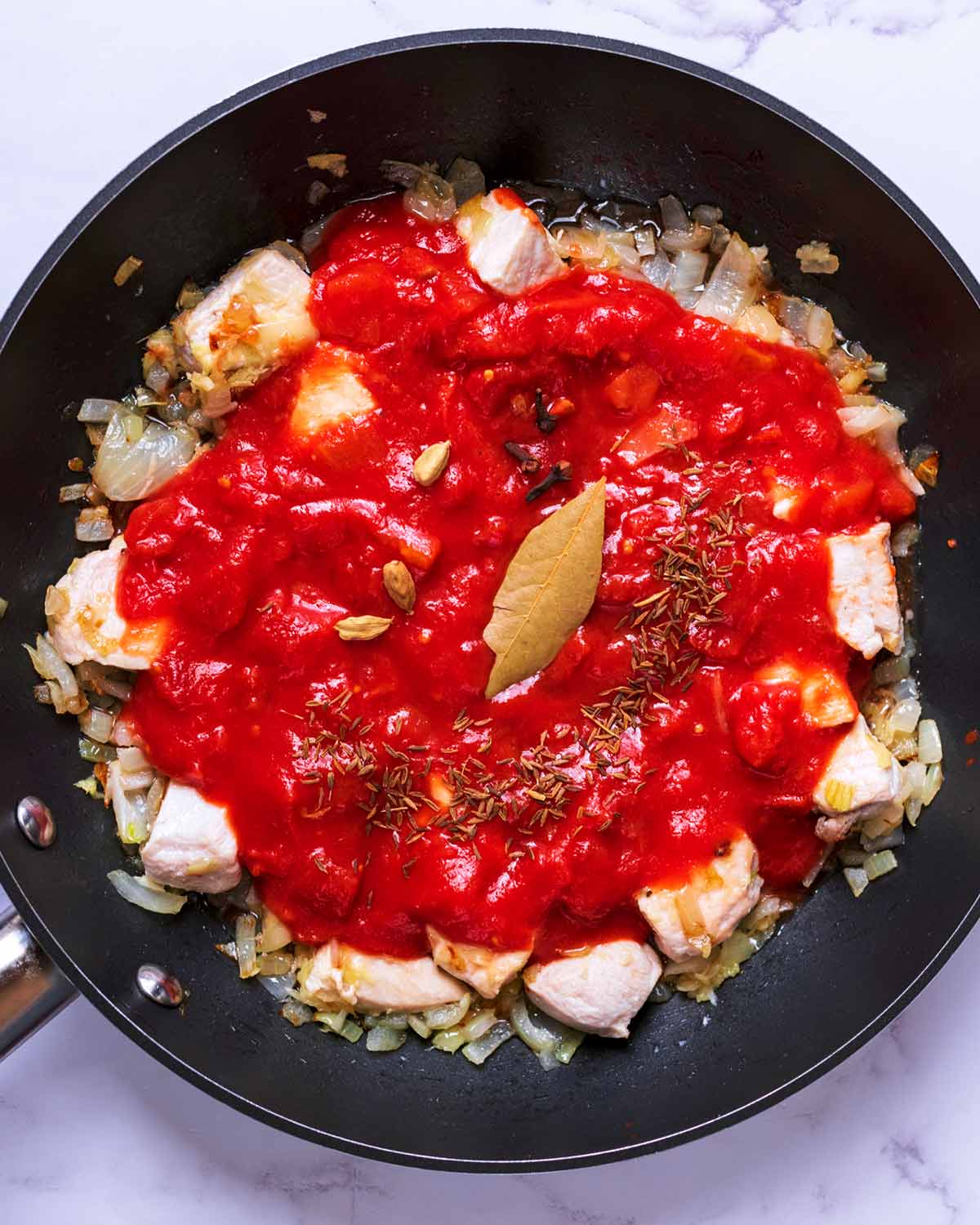 Chicken, onion, tomatoes and spices cooking in a frying pan.
