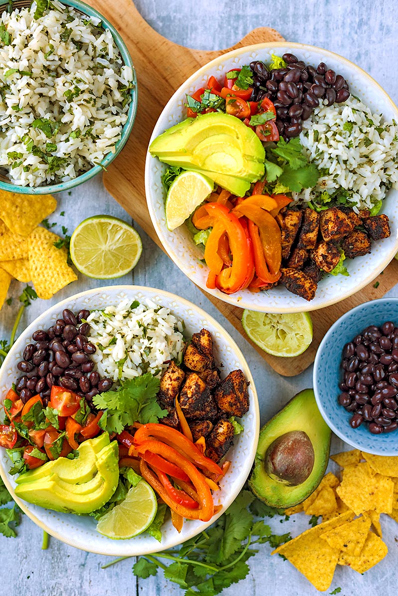 Two chicken burrito bowls next to a bowl of rice and a bowl of beans.