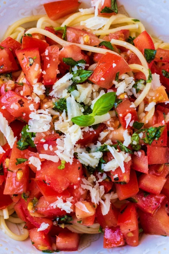 tomatoes basil leases and grated parmesan on top of spaghetti