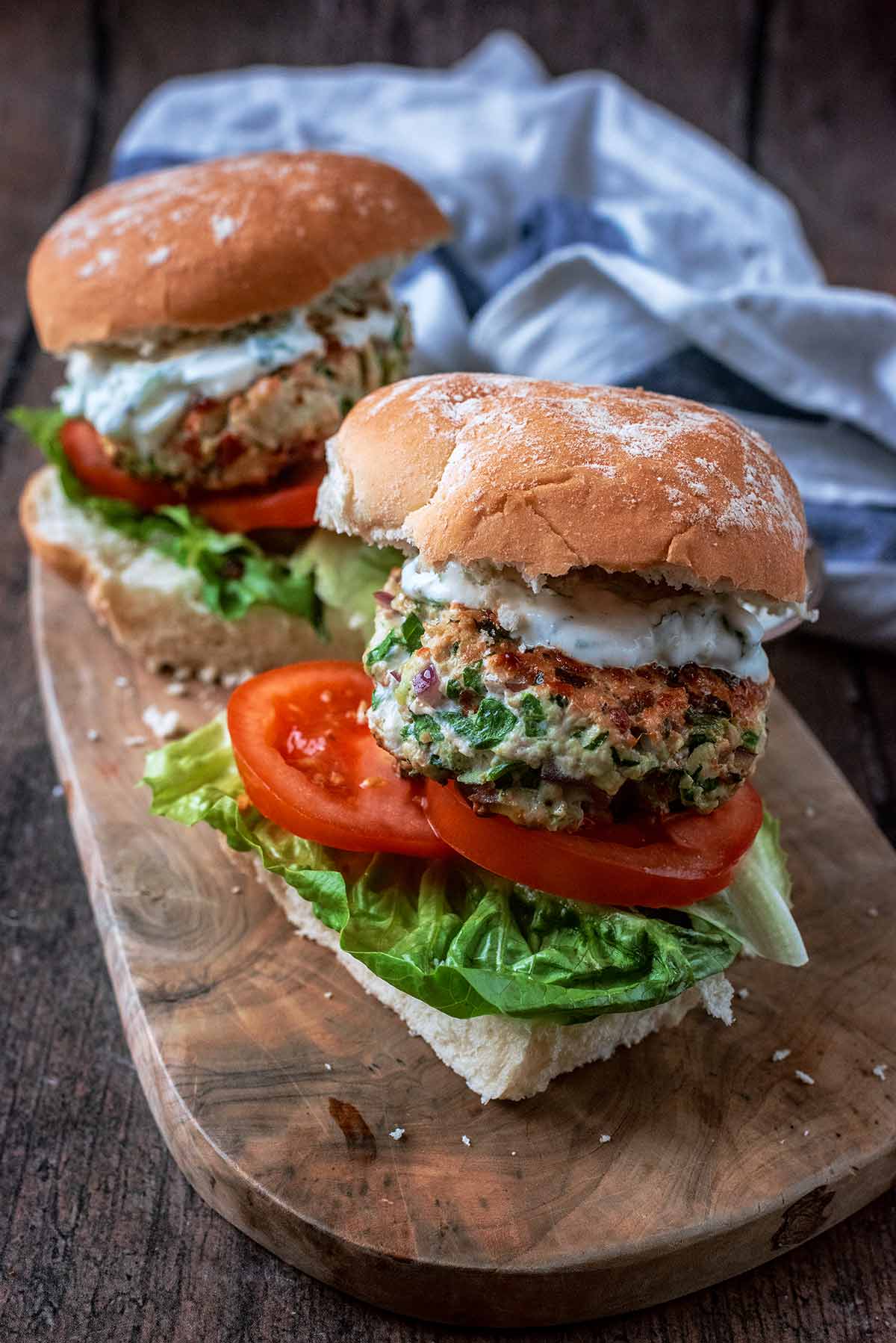 Two stacked burgers on a long wooden serving board.