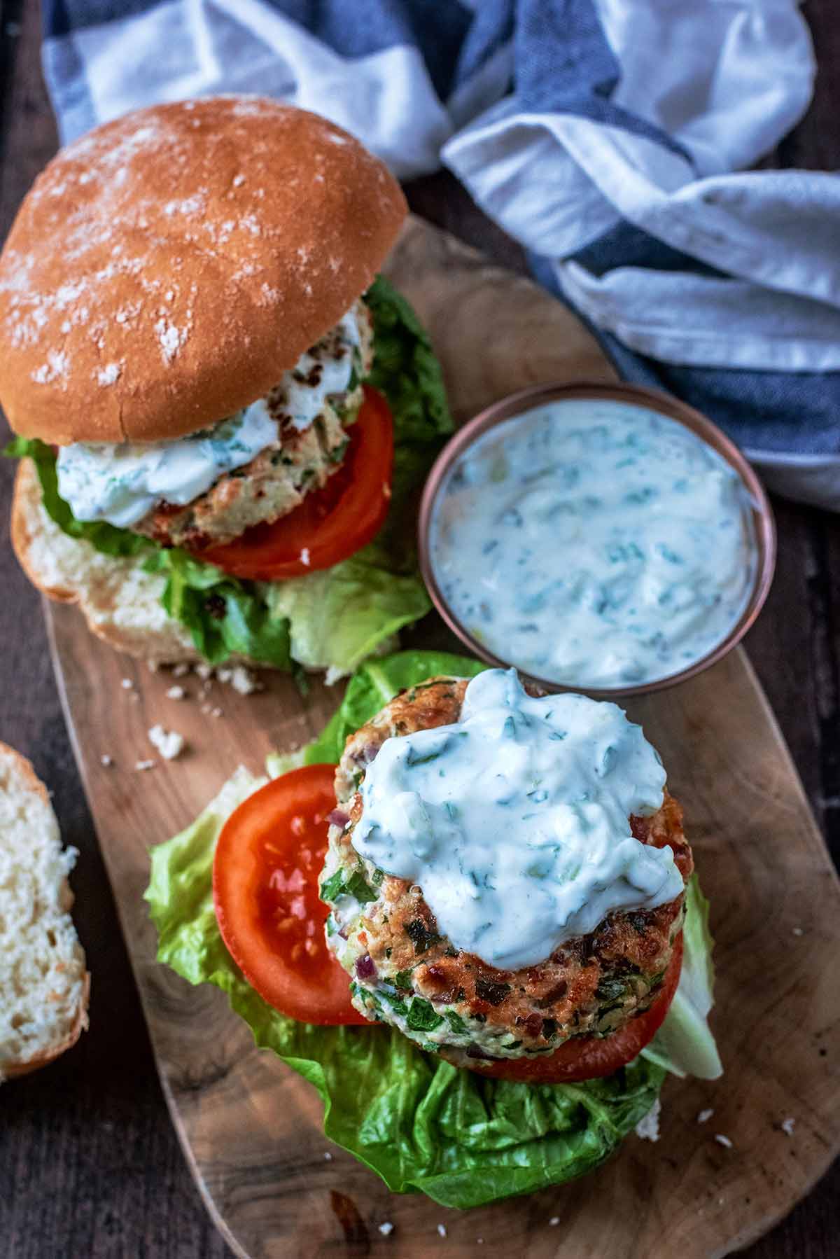 Two burgers on a serving board, one burger with the top of the bun is off.