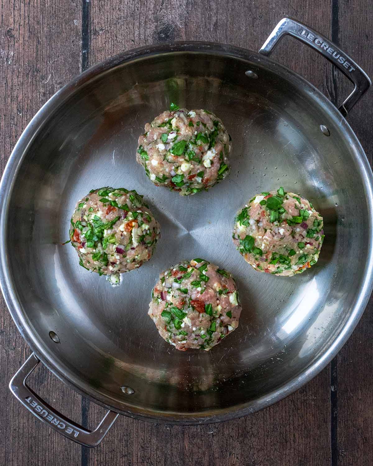 Four burger patties frying in a large pan.