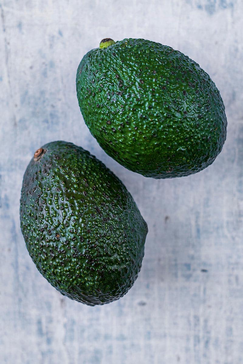 Two whole avocados on a wooden surface