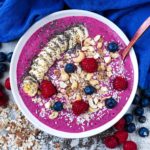 A fruit smoothie bowl topped with sliced banana, berries, nuts and oats