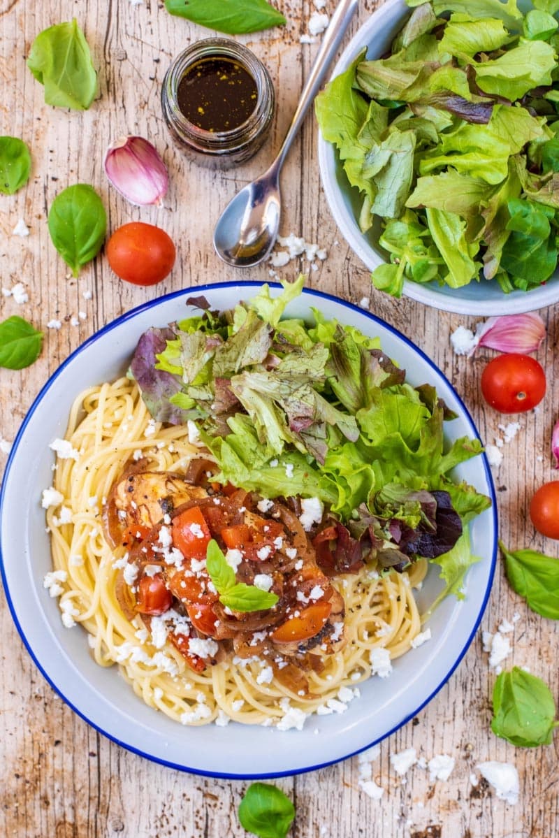 Chicken in a sauce on some spaghetti on a plate with salad.