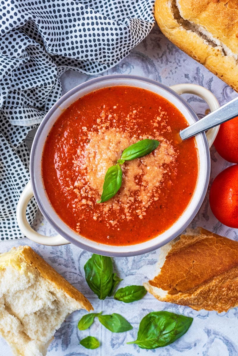A bowl of tomato soup topped with grated cheese and basil leaves.