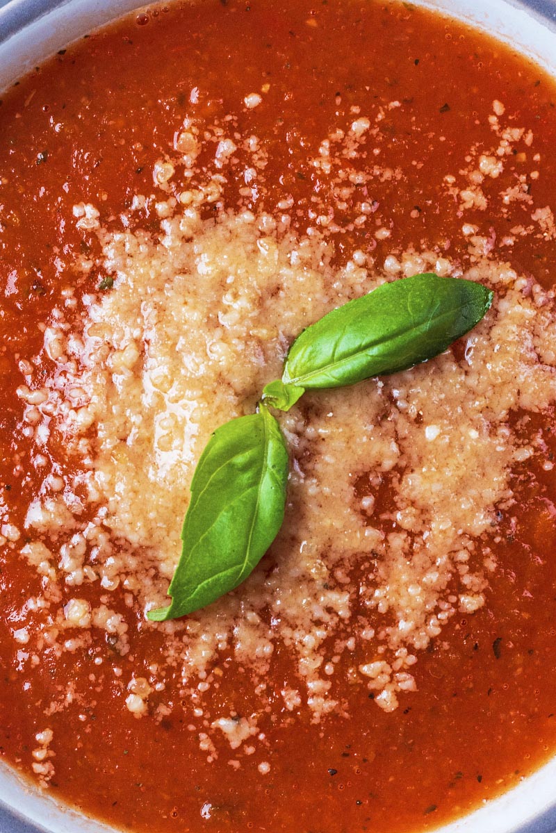 Two basil leaves and some grated cheese float on top of some tomato soup.