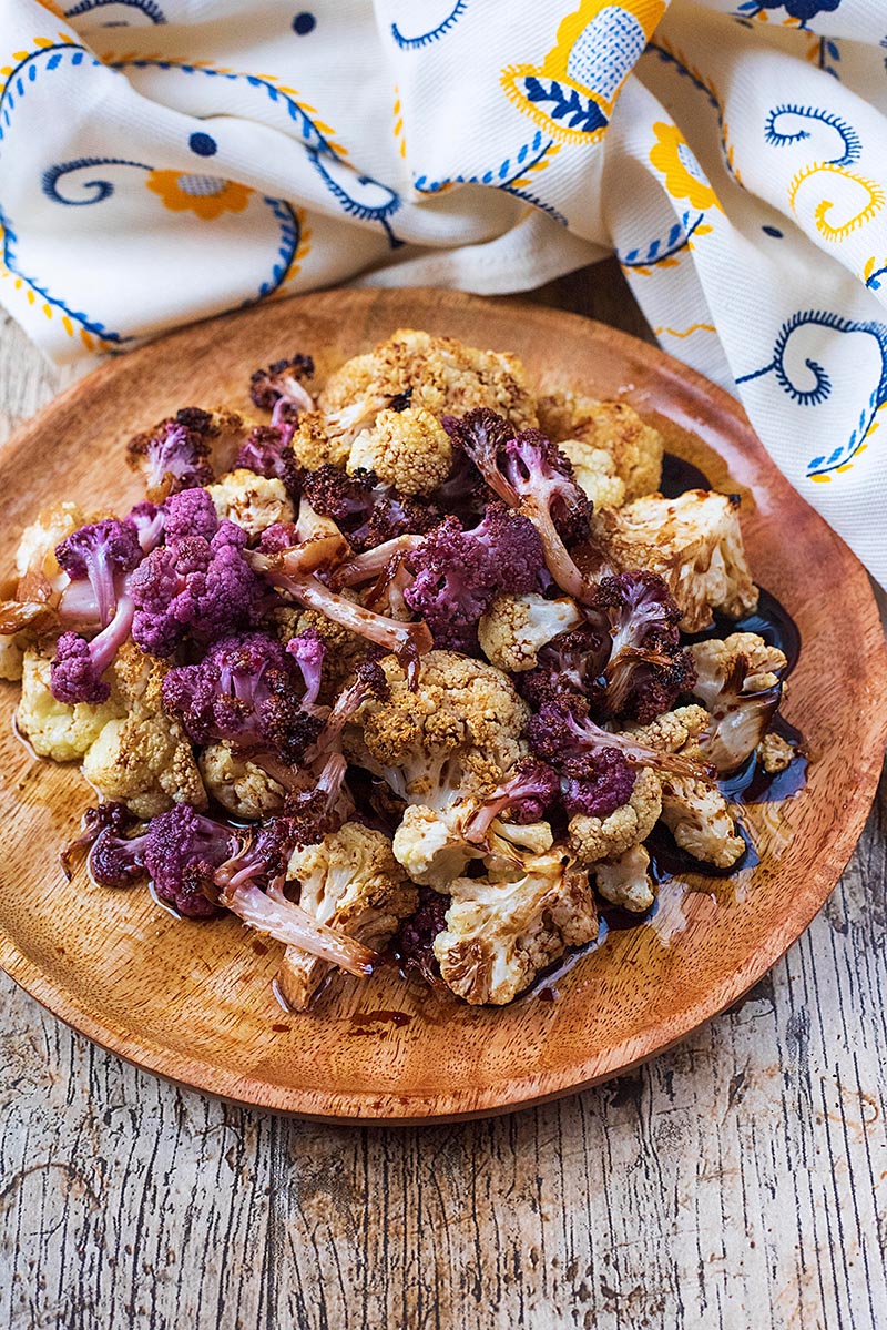 Roasted cauliflower florets on a round wooden serving plate.