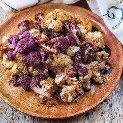 A wooden plate with white and purple roasted cauliflower on it