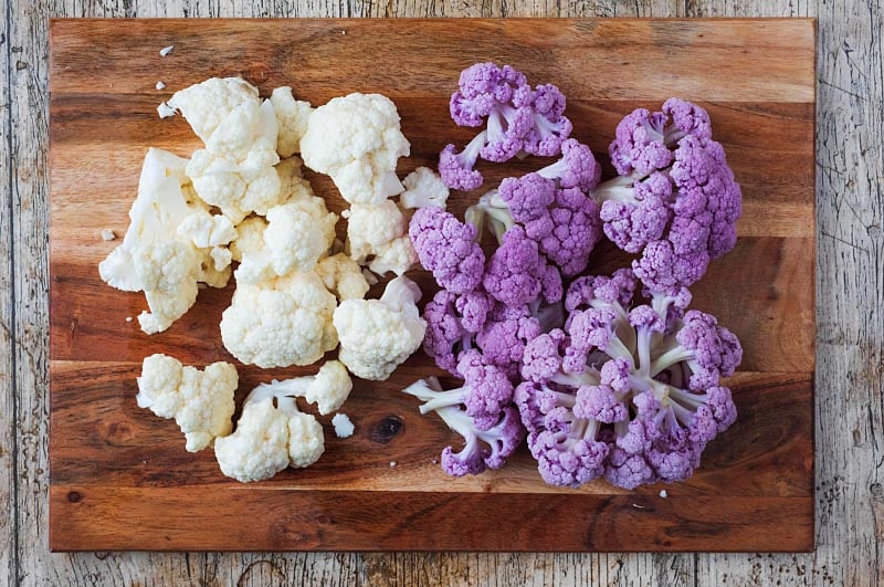 White and purple cauliflower florets on a wooden chopping board.