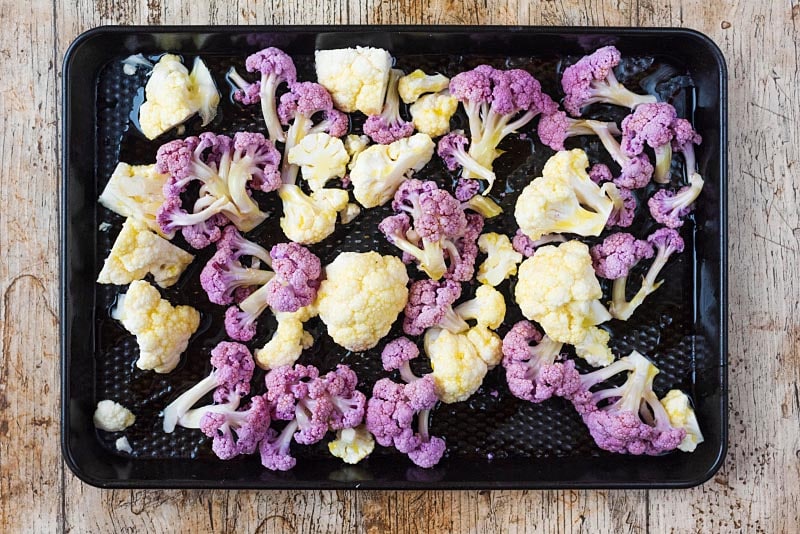 Cauliflower florets on a black baking tray.