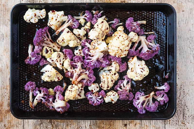 Cauliflower florets on a baking tray covered in oil, balsamic vinegar and seasoning.