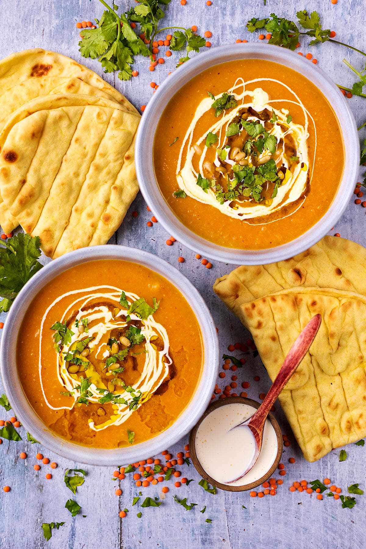 Two bowls of soup next to some flatbreads and a small bowl of cream.