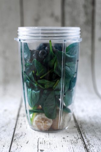 A blender jug containing banana, spinach leaves and blueberries