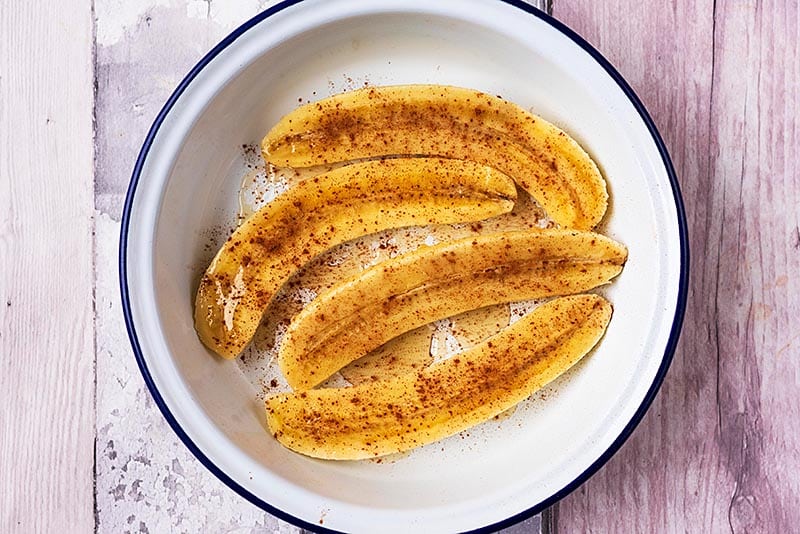 Four banana halves in a round dish covered in honey and cinnamon.