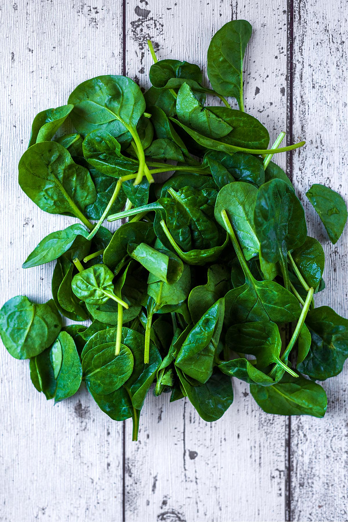 A large pile of spinach leaves on a wooden surface.