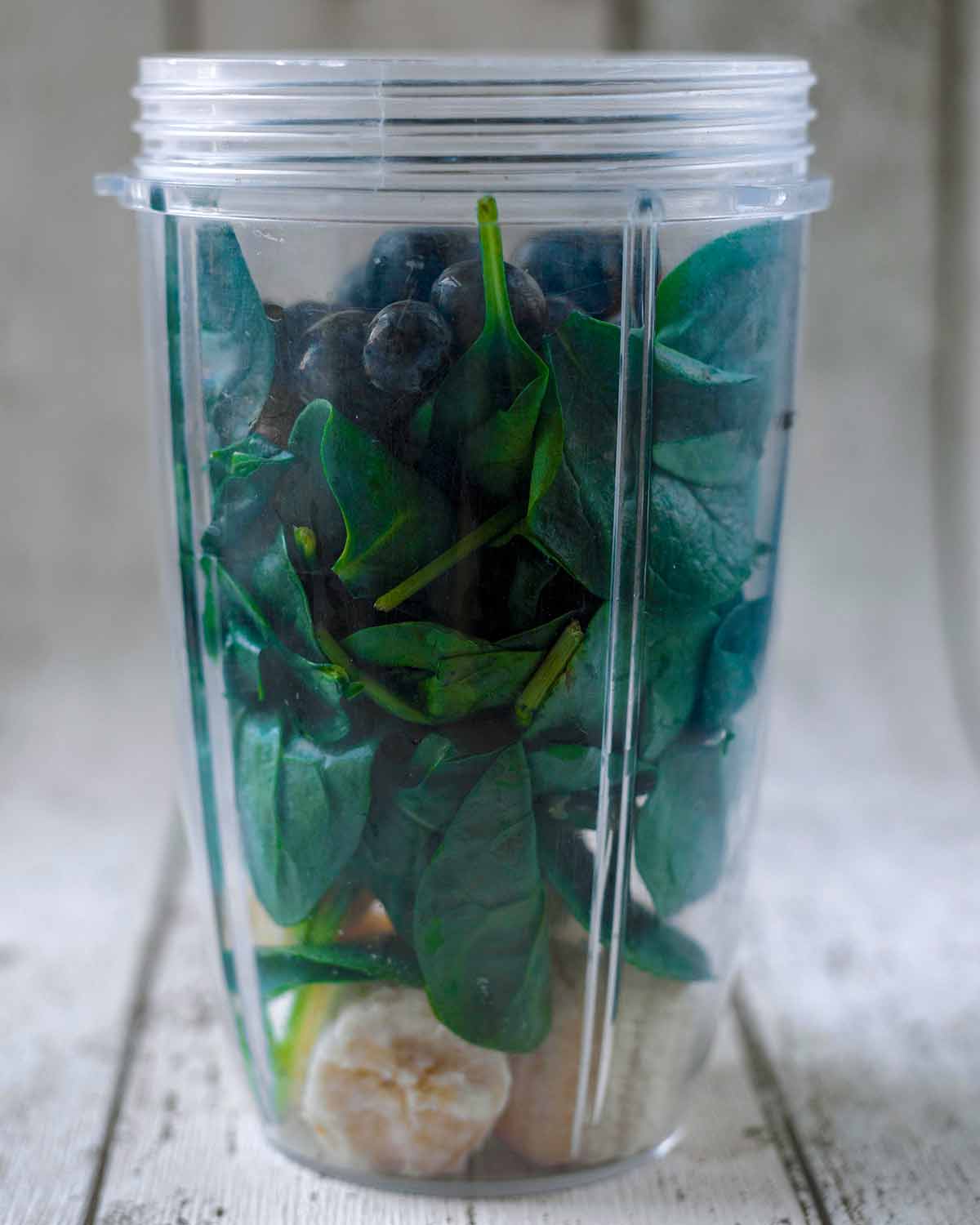 A blender jug containing banana, spinach leaves and blueberries.