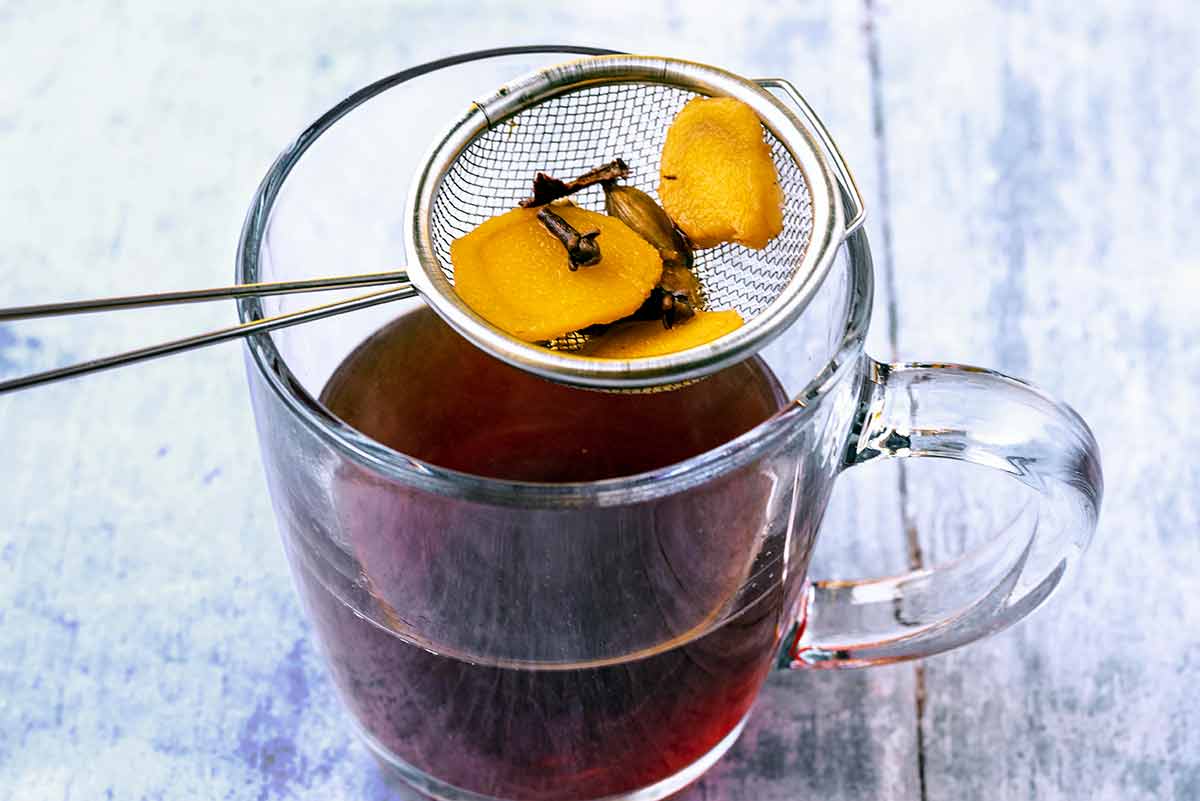 A small sieve over a glass of tea with ginger, gloves and cardamom in it.