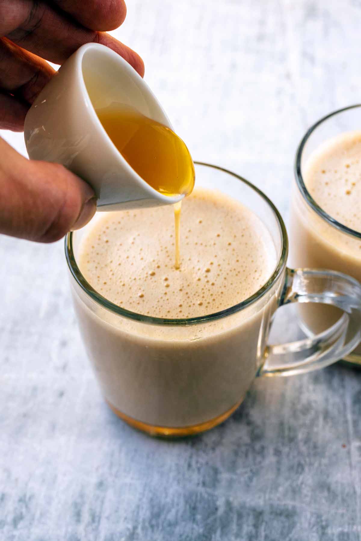 A glass of latte with honey being poured into it.