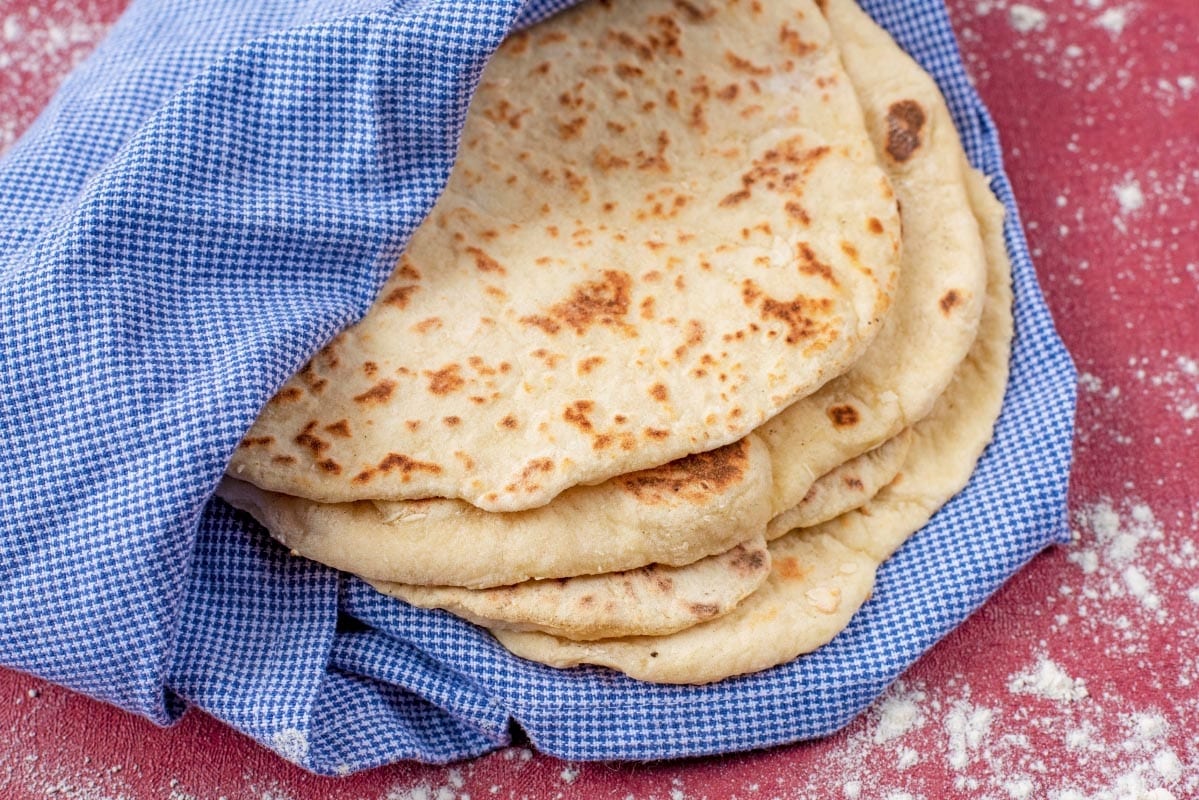 Flatbreads wrapped in a towel on a red surface.