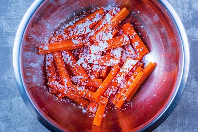 A large bowl full of carrot batons coated in cornflour.