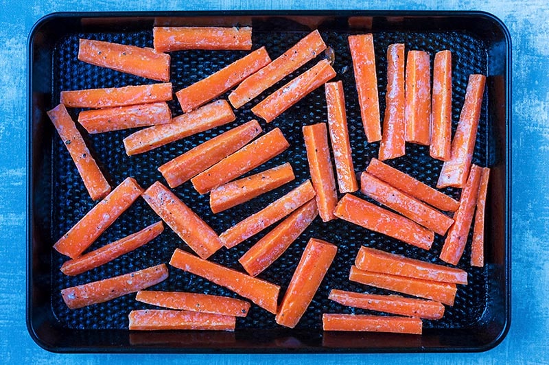 Carrot batons laid out on a black baking tray.