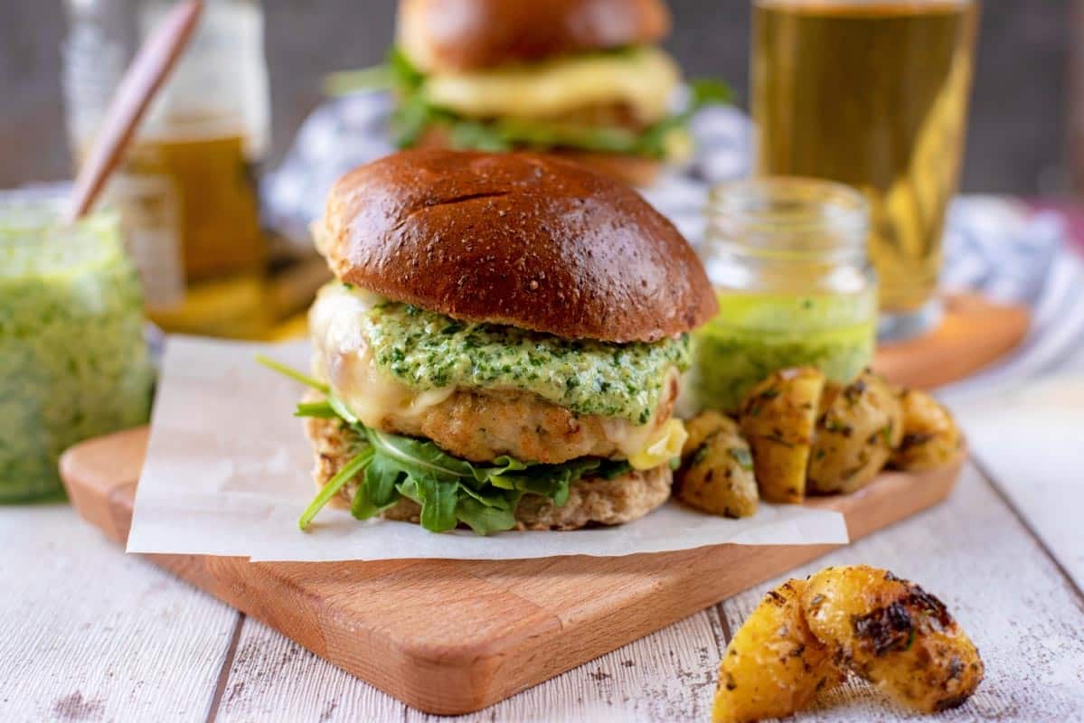 Chicken Pesto Burgers sat on a wooden serving board with potato wedges.