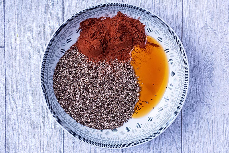 A large dish containing chia seeds, cocoa powder, maple syrup and vanilla.