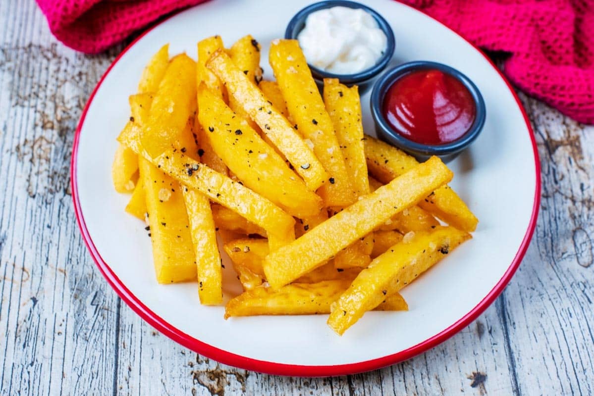 Baked Polenta Fries on a white plate with small pots of ketchup and mayonnaise.