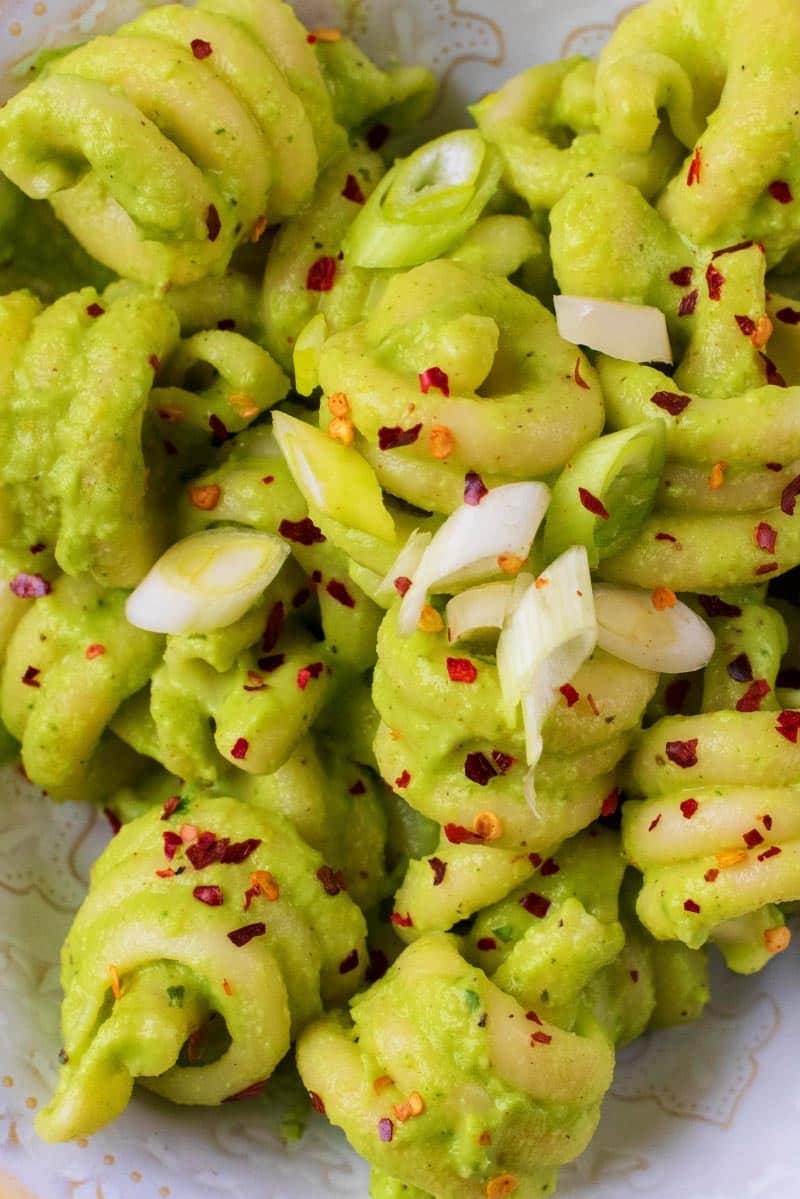 Pasta spirals in a green sauce with sliced onion and chilli flakes.