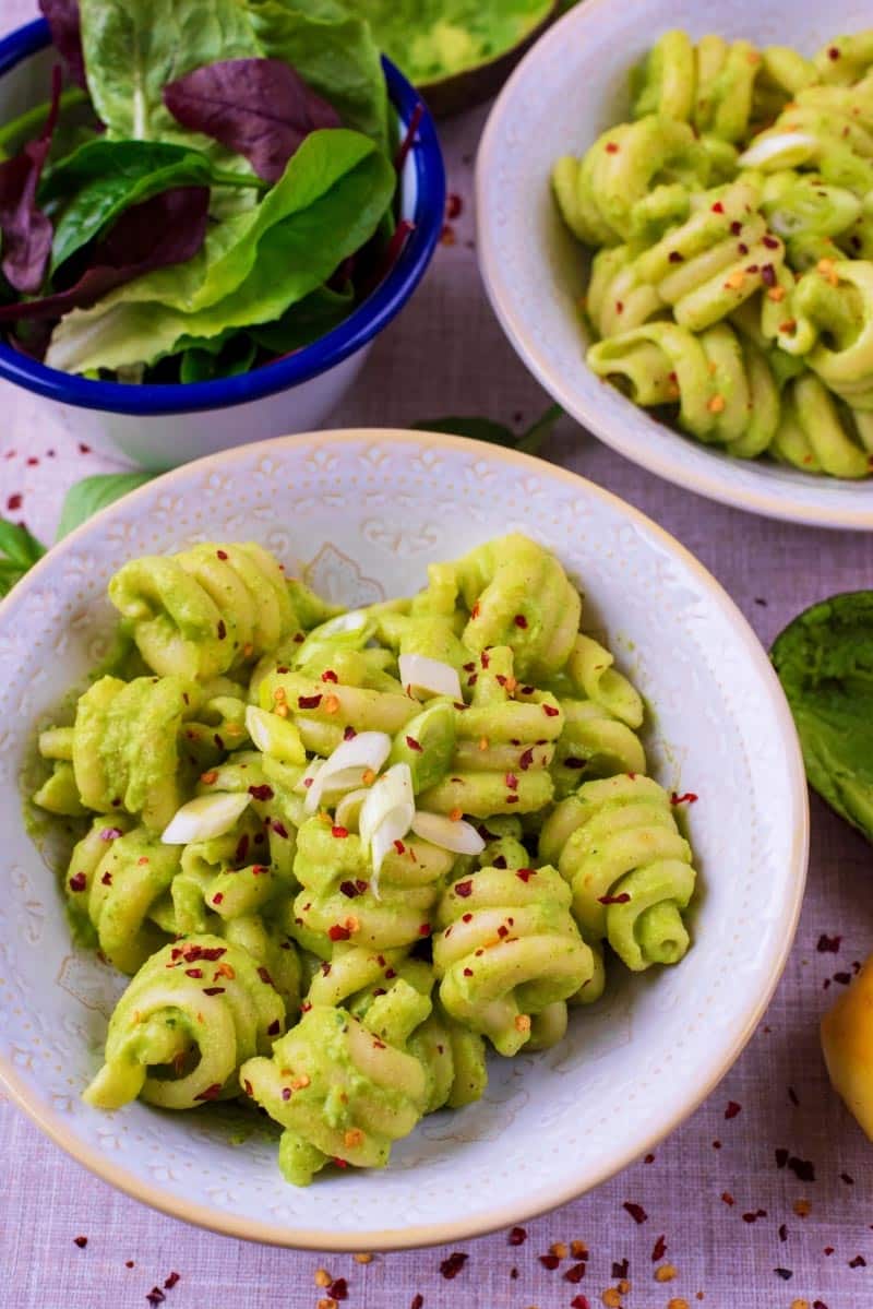 Avocado pasta in two bowls next to a side salad.