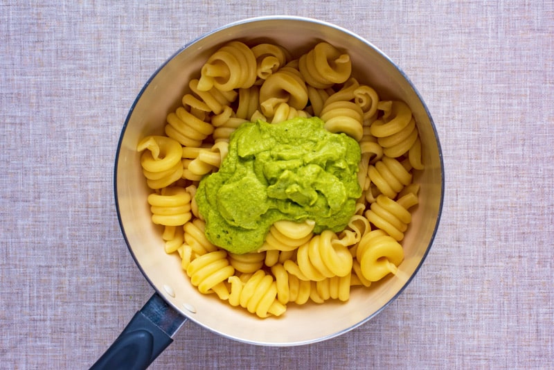 A saucepan of cooked pasta spirals with a large dollop of green sauce.