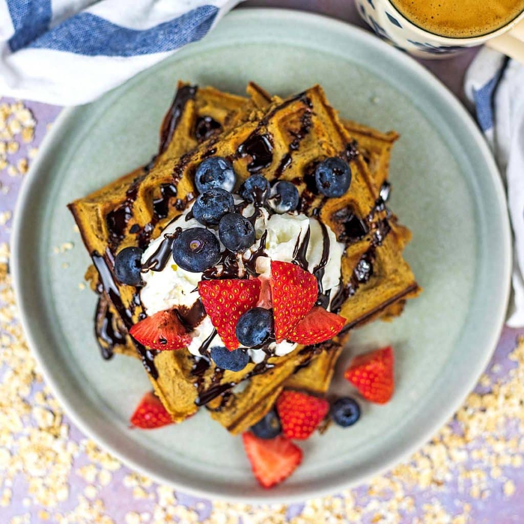 A plate of gluten free waffles topped with cream and berries.