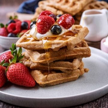 A stack of four banana oat waffles topped with yogurt and berries.
